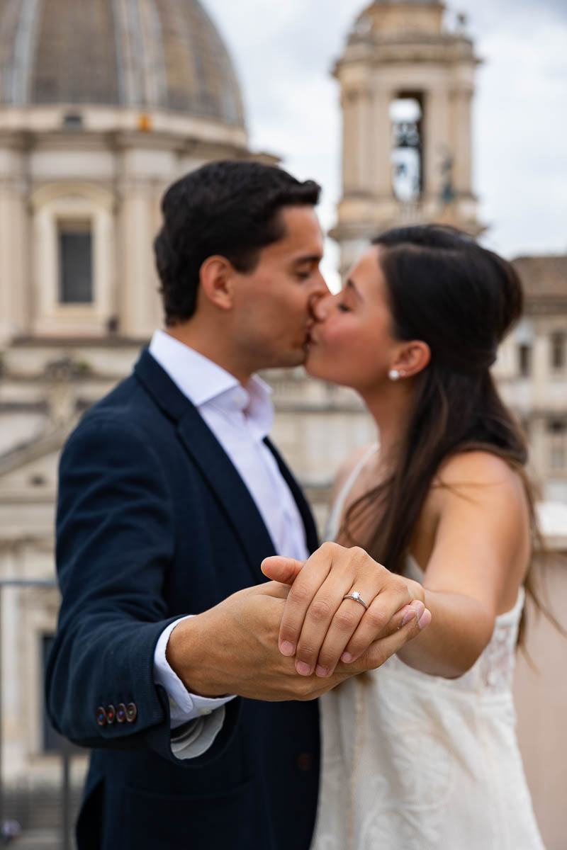 Closeup of the engagement ring with the couple kissing in the background 