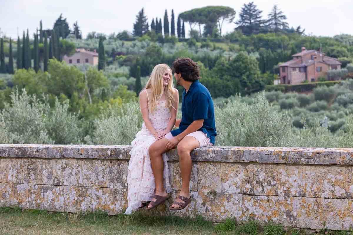 Couple sitting down on a ledge before the Tuscany countryside in the background to their proposal in Italy 