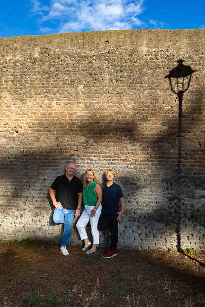 Artistic family photography taken against an ancient roman wall with the shadow of a light pole 