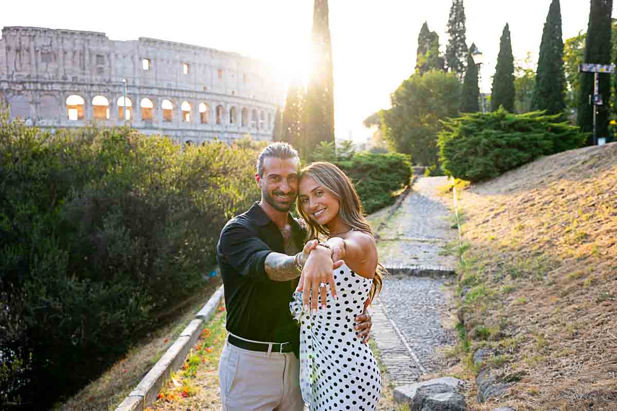 Couple together showing the engagement off to the viewer with the Coliseum as backdrop 