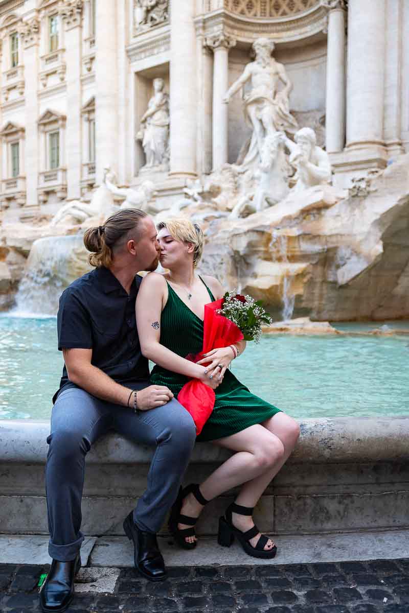 Coupe kissing on the edge of the Trevi fountain after a romantic surprise wedding proposal