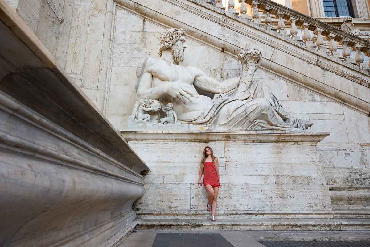 Model in red photographed before a white marble roman statue in Piazza del Campidoglio