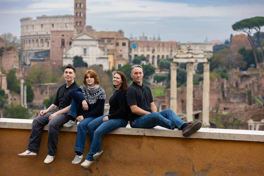 Family photography in Rome Italy picture taking while sitting down on a ledge that overlooks the roman forum and the coliseum