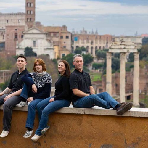 Family photography in Rome Italy picture taking while sitting down on a ledge that overlooks the roman forum and the coliseum