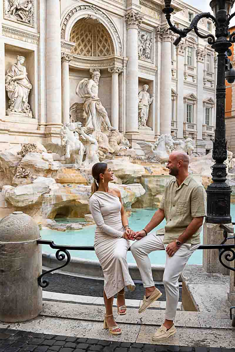 Couple sitting down at the Trevi fountain during a morning photoshoot taking San Valentine engagement photos 