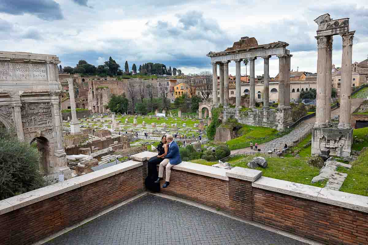 Panoramic view photo of a couple sitting down on a ledge right before the ancient roman city remains