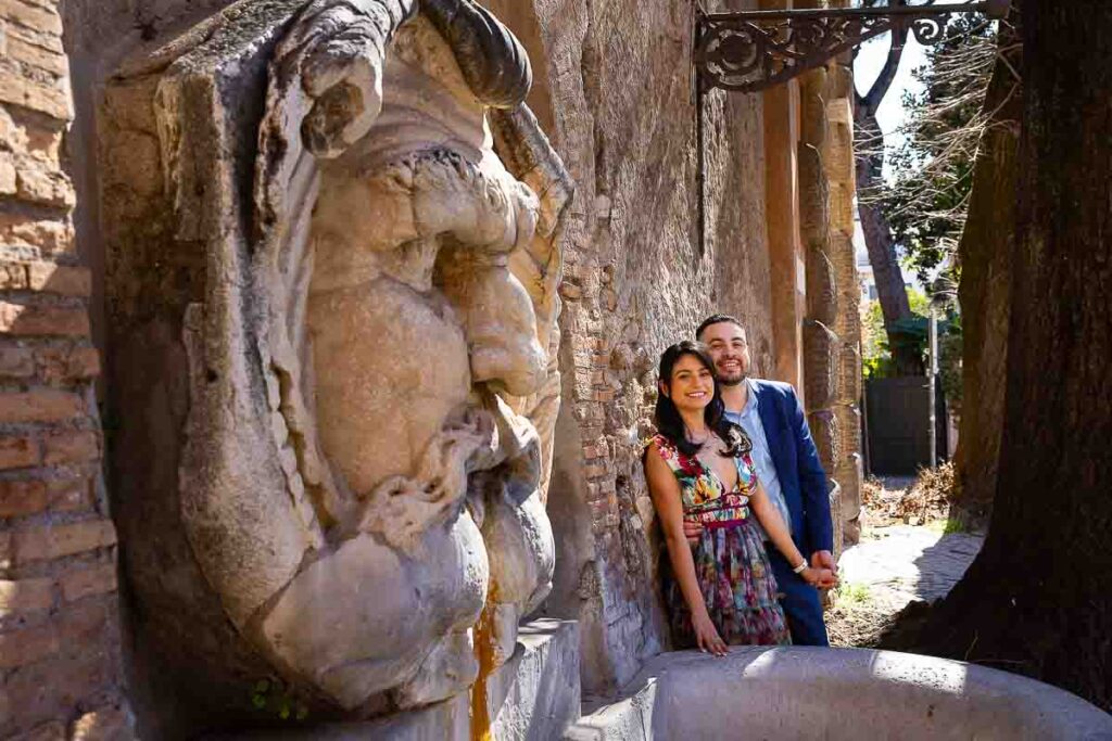 Portrait picture depicting a couple photographed by an ancient roman statue at the entrance of Giardino degli aranci